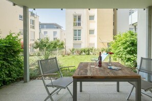 Een terras buiten met een houten tafel, twee metalen stoelen en een fles rode wijn.