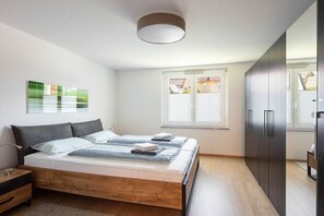 Een moderne slaapkamer met een houten bed, nachtkastje, kledingkast en een raam met zonwering.