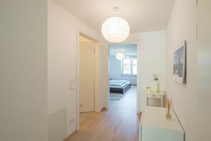 A hallway leading to a bedroom with a bed, a bedside table with a vase, and a hanging light fixture. - Holiday apartment with 1 bedroom (Überlingen)