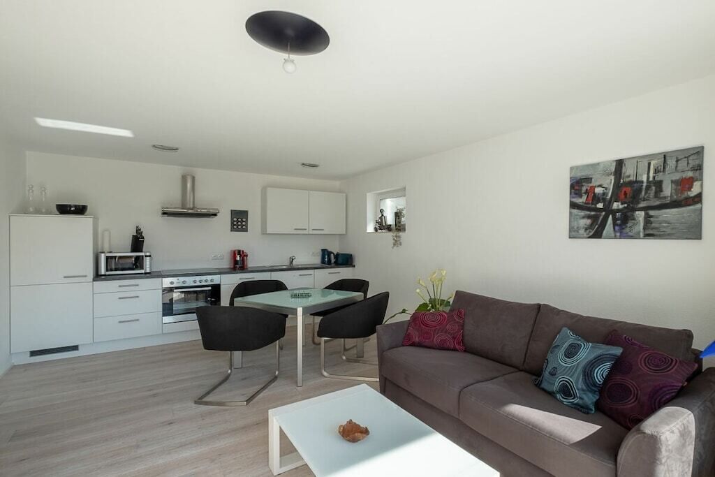 Ein moderner Wohnraum mit Essbereich, Küchenzeile und einer Couch mit Zierkissen.