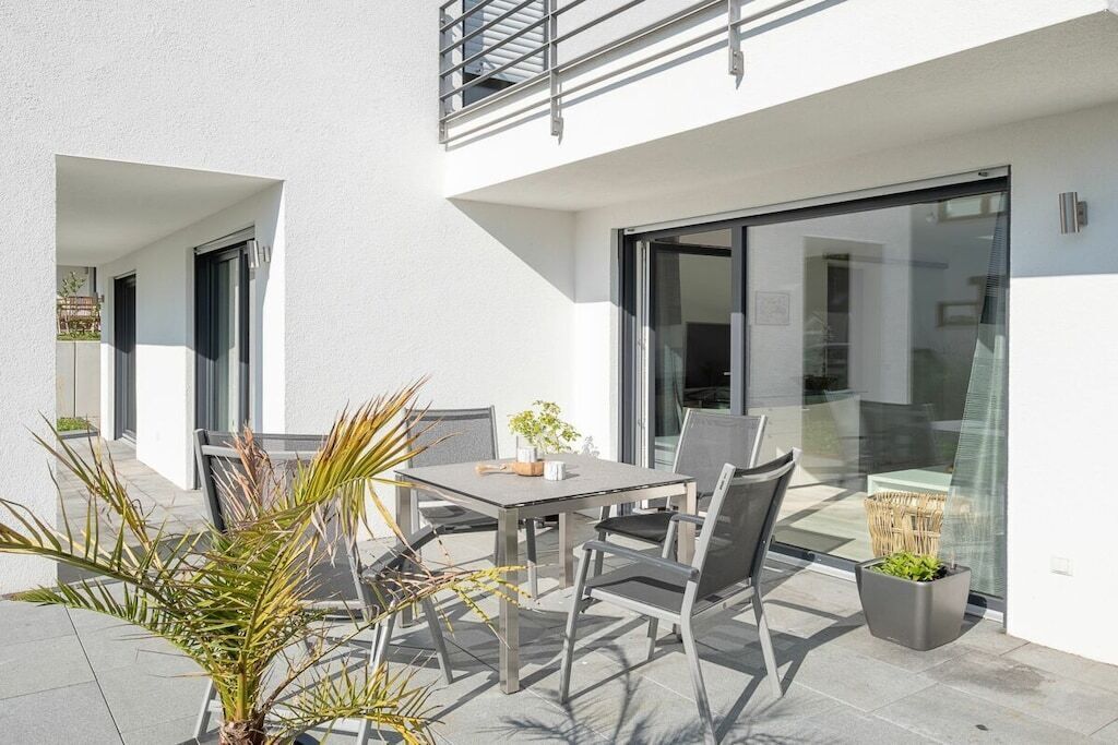Une terrasse extérieure avec une table et des chaises, un pot de fleurs et une porte vitrée donnant sur un balcon.