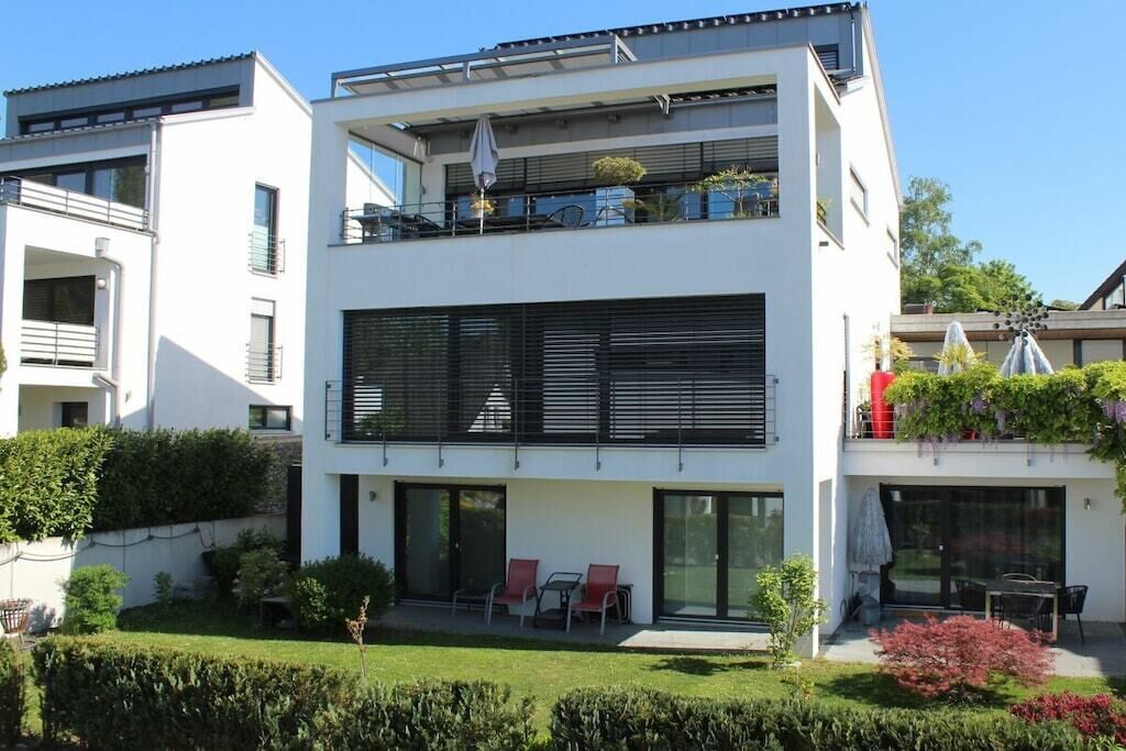 Ein modernes Wohngebäude mit zwei Etagen, einem Balkon, einer überdachten Außenlounge und einem gepflegten Garten.