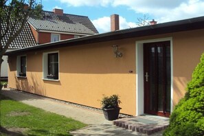 Ein einstöckiges Haus mit einer braunen Fassade, einer Haustür und einem kleinen Vorgarten mit einem Blumentopf.