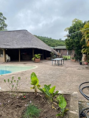 A pool area with a thatched-roof structure, a table, and potted plants. - Room-thornycroft Lodge & Spa Kugompo Cit (East London)