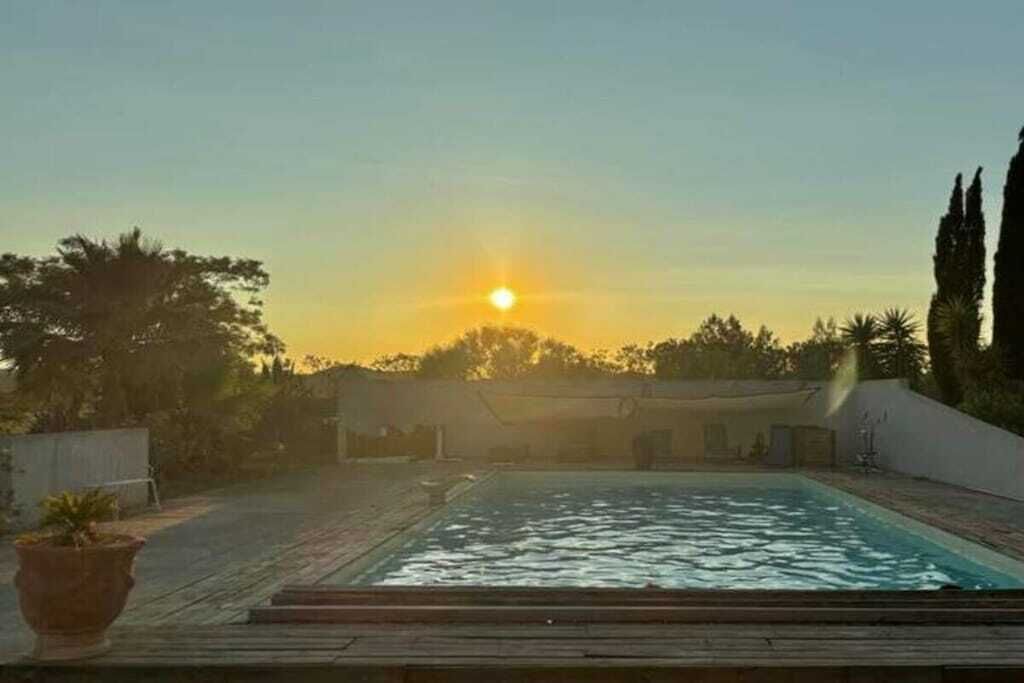 A swimming pool with a wooden deck and a view of the sunset.