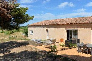 A single-story building with a tiled roof, a patio with outdoor furniture, and a small garden area. - Gîte Pomme de Pin 2/4 personnes (LEZIGNAN CORBIERES)