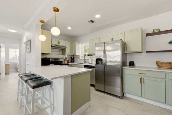 A modern kitchen with a central island, stainless steel appliances, and light-colored cabinetry. - Venice Island Florida pool Home (Venice)