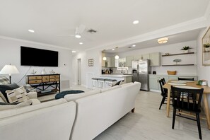 A modern living room with a sofa, a television, and a dining area with a table and chairs. - Venice Island Florida pool Home (Venice)