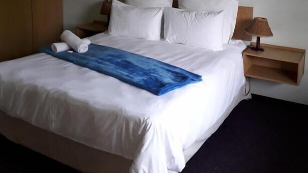 Quarto de hotel com cama grande, mesa de cabeceira com abajur e obra de arte na parede.