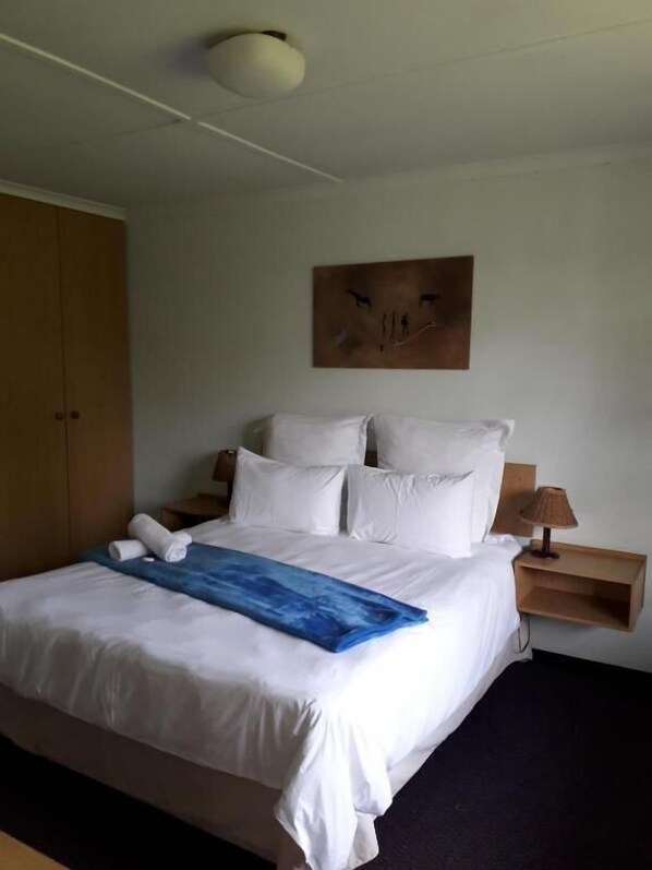 A hotel room with a large bed, a bedside table with a lamp, and a wall-mounted artwork. - Room-thornycroft Lodge & Spa Kugompo (East London)