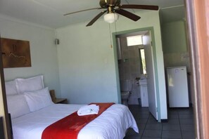 A hotel room with a bed, a ceiling fan, a bathroom with a toilet and sink, and a kitchenette with a refrigerator. - Room-thornycroft Lodge & Spa Kugompo (East London)