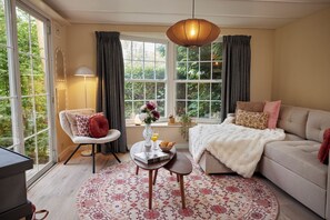 Ein helles Zimmer mit einer Couch, einem Sessel und einem runden Tisch mit einer Vase und einem Buch.
