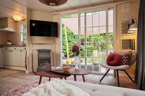 A cozy living room with a fireplace, a television mounted above it, and a dining area with a table set for two. - 4P Modern Chalet with Private Sauna - Fenced Forest Garden (Putten)