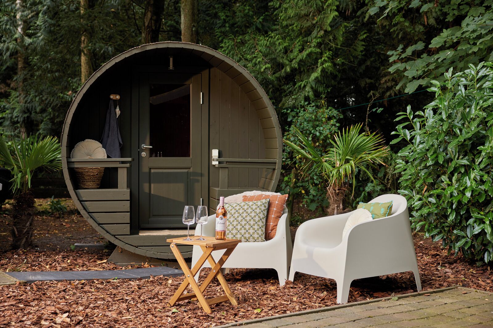 A cozy outdoor seating area with a round wooden structure, a table with glasses and a bottle, and white chairs with cushions.