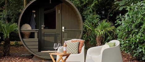 Een gezellig buitengebied met een ronde houten constructie, een tafel met glazen en een fles, en witte stoelen met kussens.