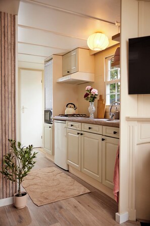 A kitchen with a stove, sink, cabinets, and a vase with flowers. - 4P Modern Chalet with Private Sauna - Fenced Forest Garden (Putten)