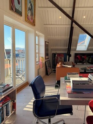 A spacious room with a high ceiling, large windows, a seating area with a sofa and armchairs, a bookshelf, and a dining table. - Top-floor flat by the harbour in Henningsvær (Henningsvær)