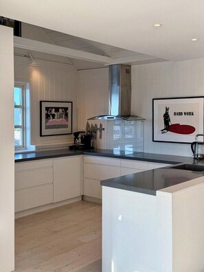 A modern kitchen with white cabinetry, a central island, and a stainless steel range hood. - Top-floor flat by the harbour in Henningsvær (Henningsvær)