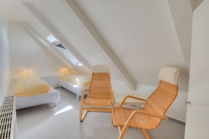A small, modern room with a sloped ceiling, two single beds, and two wicker chairs. - Holiday apartment in Sylt with 1 bedroom (Wenningstedt)