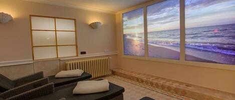 Ein Zimmer mit großem Fenster und Meerblick, einer Massageliege und einem an der Wand befestigten Regal.