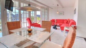 Uma sala de estar moderna com uma mesa de jantar de vidro, sofás vermelhos e cadeiras de vime.