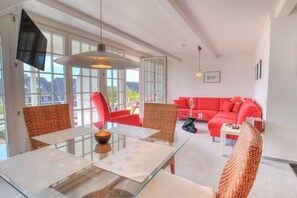 A modern living room with a glass dining table, red sofas, and wicker chairs. - Holiday apartment in Sylt with 1 bedroom (Wenningstedt)