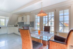 Une cuisine moderne avec des meubles blancs, une table à manger en verre, des chaises en osier et un luminaire suspendu.