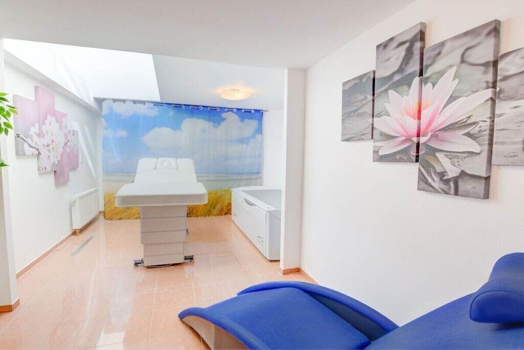 Ein Behandlungsraum mit einer Liege, einem Schreibtisch und einem an der Wand hängenden Kunstwerk.