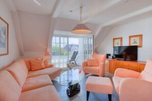 A modern living room with a glass coffee table, a sofa, and a television on a wooden cabinet. - Holiday apartment in Sylt with 1 bedroom (Wenningstedt)