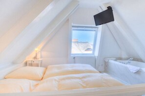 Un dormitorio con cama, ventana, mesita de noche y televisor de pared.
