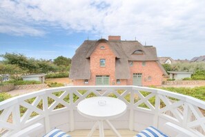 Una casa con techo de paja y paredes de ladrillo, un porche blanco con mesa y sillas, y vistas del paisaje circundante.