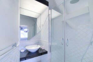 Un baño moderno con cabina de ducha de vidrio, lavamanos blanco y encimera negra.