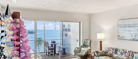 A room with a view of the sea, a chair, a sofa, and a table.