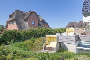 Een huis met een opvallend gebogen dak en een tuin met een houten terras en twee streepstoelen.