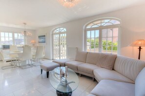 A modern living room with a glass coffee table, a beige sofa, and a dining area with white chairs. - Holiday apartment in Sylt with 1 bedroom (Wenningstedt)