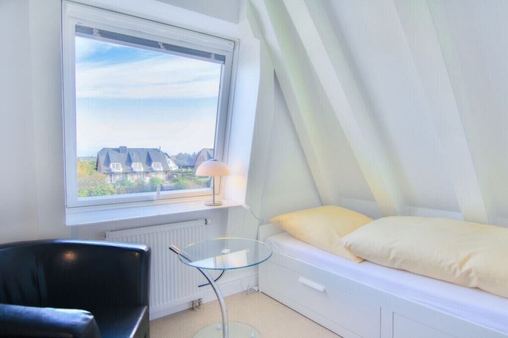 Et soveværelse med seng, stol, bord og et vindue med udsigt til huse.