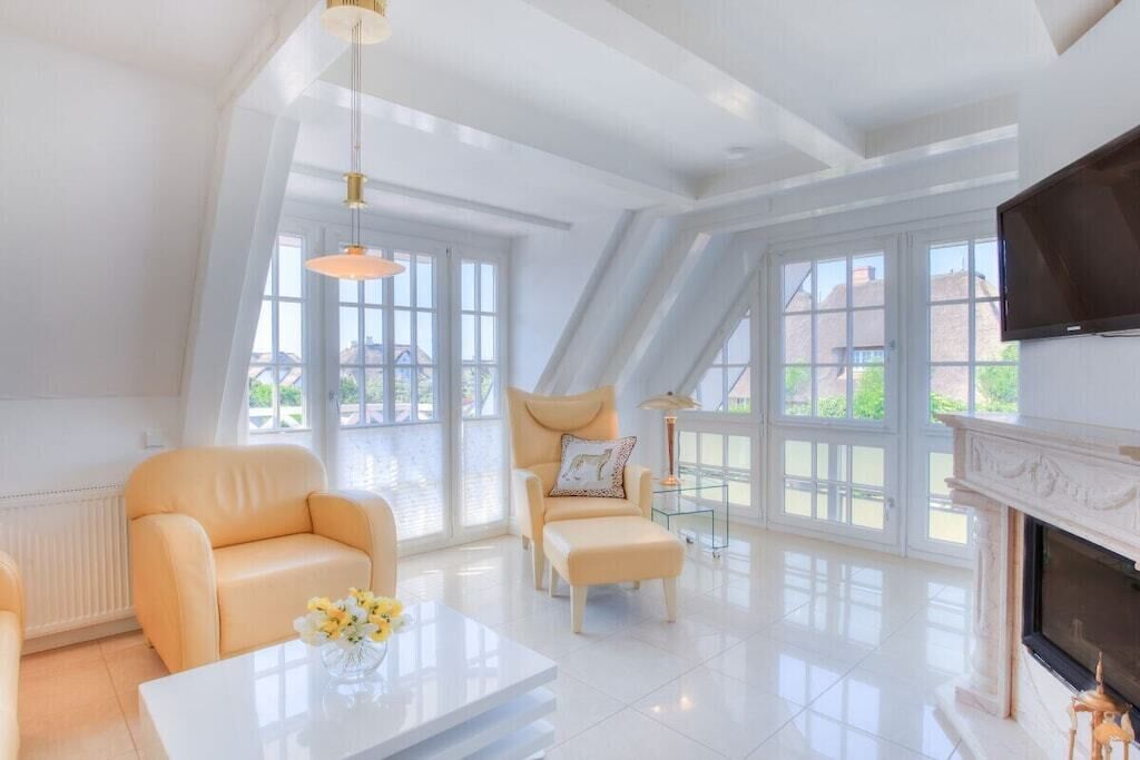 A spacious living room with a fireplace, large windows, and a modern chandelier.