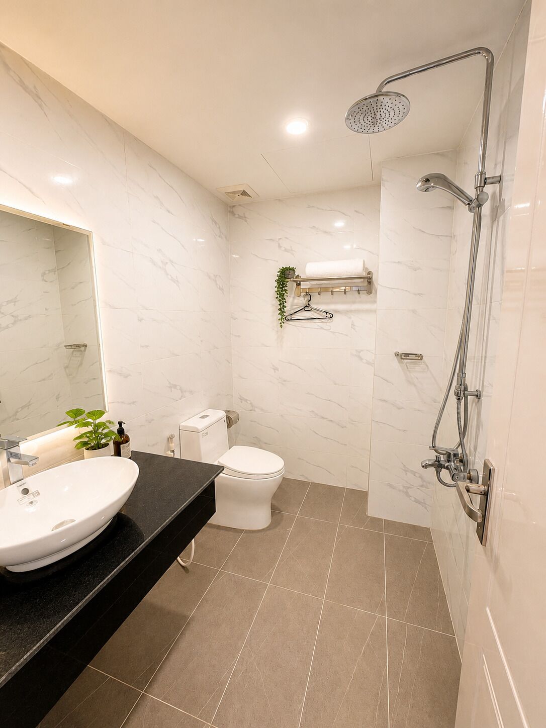 A modern bathroom with a white marble sink, a toilet, and a shower with a handheld showerhead.