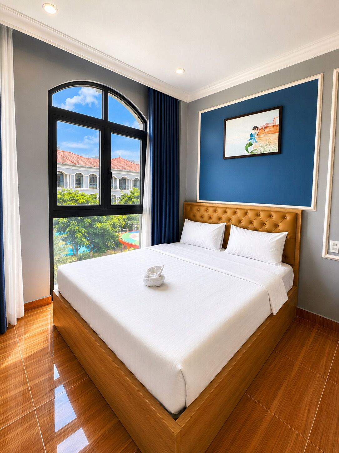 A hotel room with a large bed, a view of a building with a red roof, and a painting on the wall.