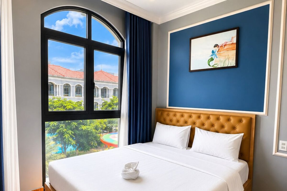 A hotel room with a large bed, a view of a building with a red roof, and a painting on the wall.