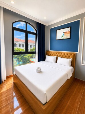 A hotel room with a large bed, a view of a building with a red roof, and a painting on the wall. - InaVay Retreat | 2 mins walk to Beach | Heart of Grand World, Phu Quoc (Phu Quoc)