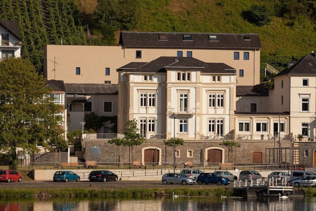 Un edificio de varios pisos con un patio central, rodeado de coches estacionados y una masa de agua con un puente.