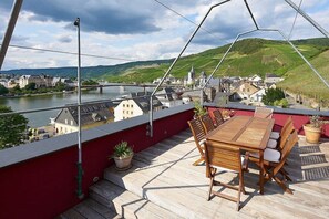 Een houten terras met een tafel en stoelen, met uitzicht op een rivier en stad.