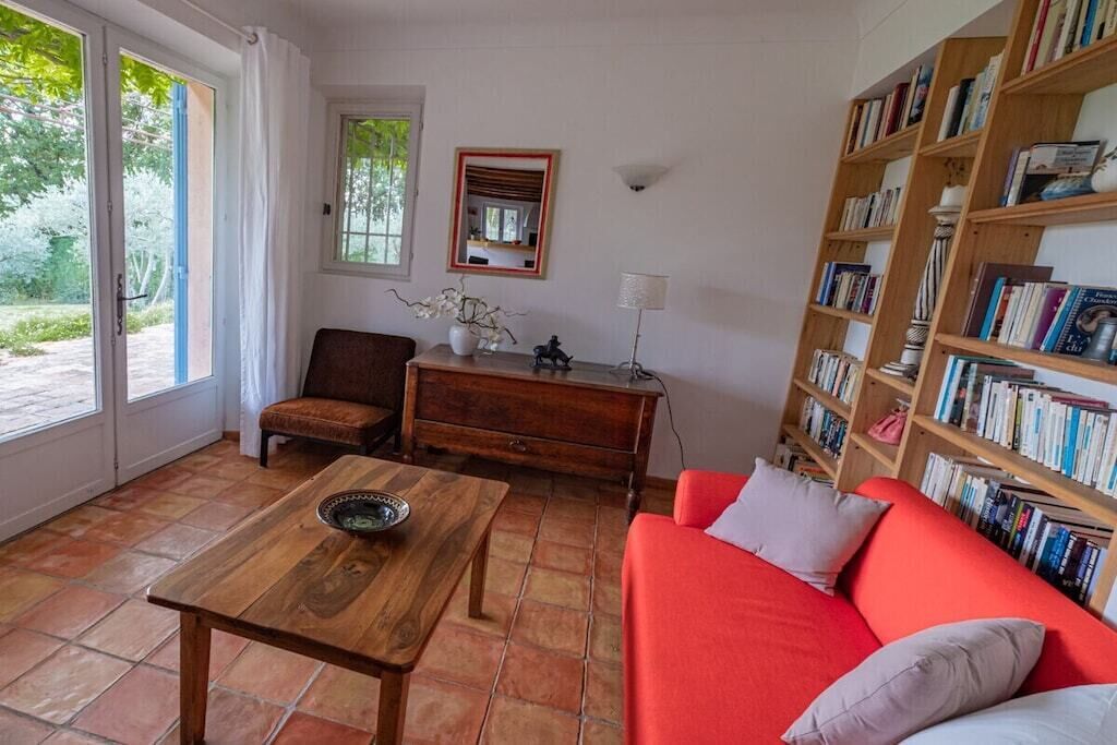 A room with a red sofa, a wooden coffee table, a chair, a bookshelf, and a window with curtains.