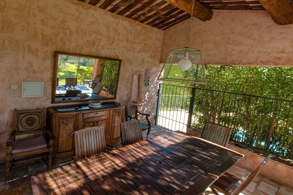 A room with a wooden table, chairs, a mirror, and a hanging light fixture.