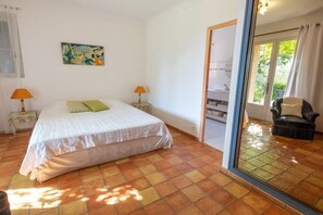 Ein Schlafzimmer mit einem Bett, zwei Nachttischlampen, einem Gemälde und Blick durch eine Glastür auf einen Außenbereich.
