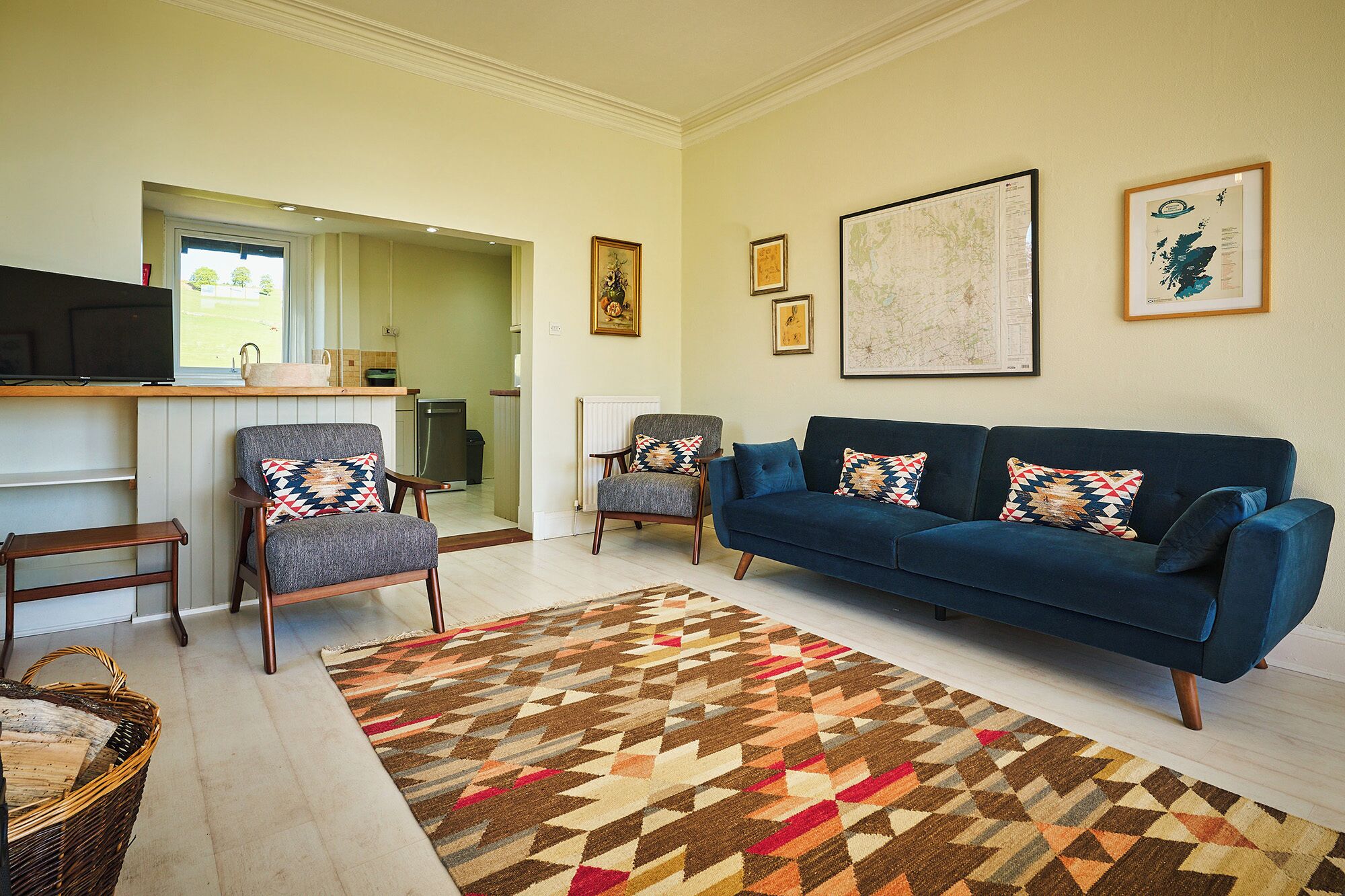 A living room with a blue sofa, two armchairs, a patterned rug, and a television on a stand.