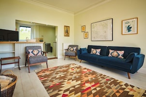 Una sala de estar con un sofá azul, dos sillones, un tapete estampado y un televisor sobre un mueble.