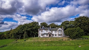 A large, historic house with multiple chimneys, surrounded by lush green fields and dense trees. - Kinclune House & Cottages - Sleeps 28 (Kirkton of Kingoldrum)
