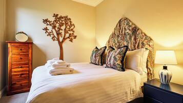 Una cama bien hecha con un cabecero con forma de árbol, un aparador de madera y una lámpara en una mesita de noche.